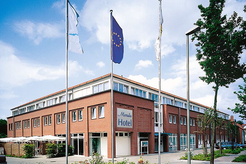 Architektonische Landschaft mit organischem Betongebäude Moderner, organisch geformter Betonbau mit Fußgängern auf einer Brücke und einem Teich im Vordergrund.